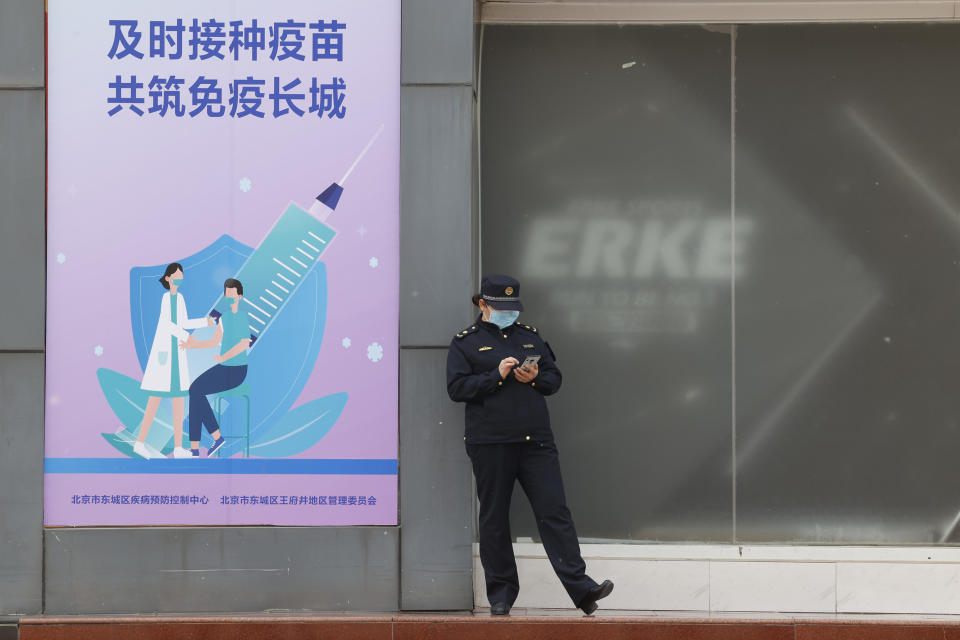 A uniformed worker stands outside a coronavirus vaccination site with a board displaying the slogan, "Timely vaccination to build the Great Wall of Immunity together" in Beijing on Friday, April 9, 2021. China's success at controlling the outbreak has resulted in a population that has seemed almost reluctant to get vaccinated. Now it is accelerating its inoculation campaign by offering incentives — free eggs, store coupons and discounts on groceries and merchandise — to those getting a shot. (AP Photo/Ng Han Guan)