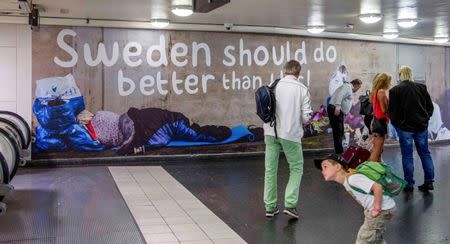 People stand near a poster put up by the Sweden Democrats political party showing homeless people at the Ostermalmstorg subway station in Stockholm, Sweden, in this August 3, 2015 file photo. REUTERS/Bertil Ericson/TT News Agency/Files