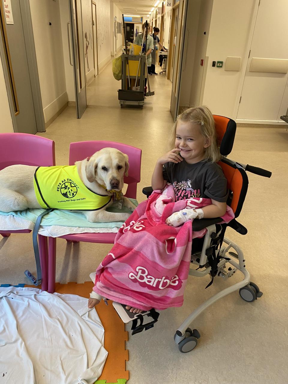 Evie sitting in a wheelchair in hospital with a service dog. 