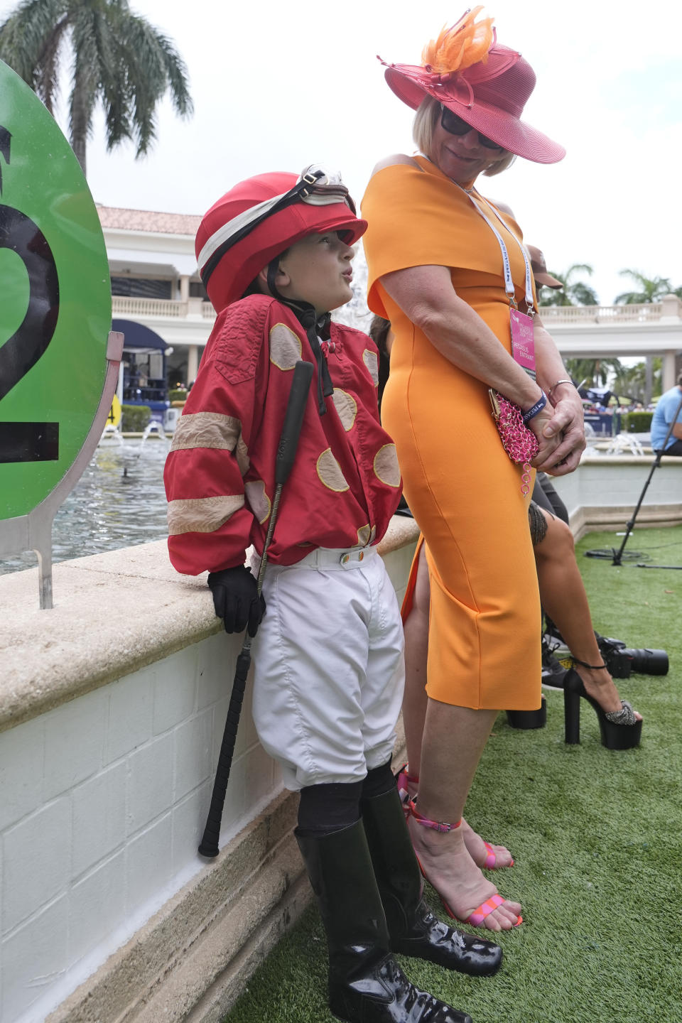 Dressed as a jockey, Rocco Joseph, 7, son of trainer Saffie Joseph, waits for the horses in the paddock with his aunt Senta Mackel, before a horse race during the Pegasus World Cup Day, Saturday, Jan. 27, 2024, at Gulfstream Park in Hallandale Beach, Fla. (AP Photo/Wilfredo Lee)