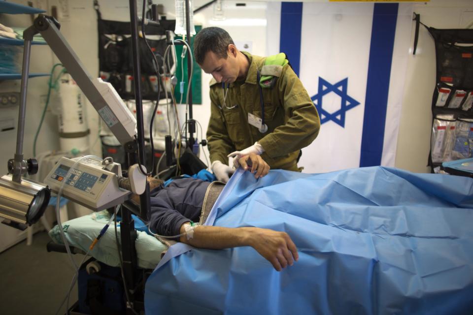 Israeli military medic tends a Syrian man who was wounded in the ongoing violence in Syria, in a military hospital located in the Golan Heights near the border with Syria on Tuesday, Feb. 18, 2014. Since the Syrian conflict erupted almost three years ago hundreds of Syrians have received treatment in Israeli hospitals.(AP Photo/Menahem Kahana, Pool)