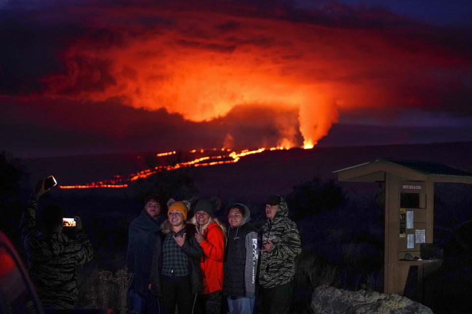 People pose for a photo in front of lava erupting from Hawaii's Mauna Loa volcano Wednesday, Nov. 30, 2022, near Hilo, Hawaii. (AP Photo/Gregory Bull)