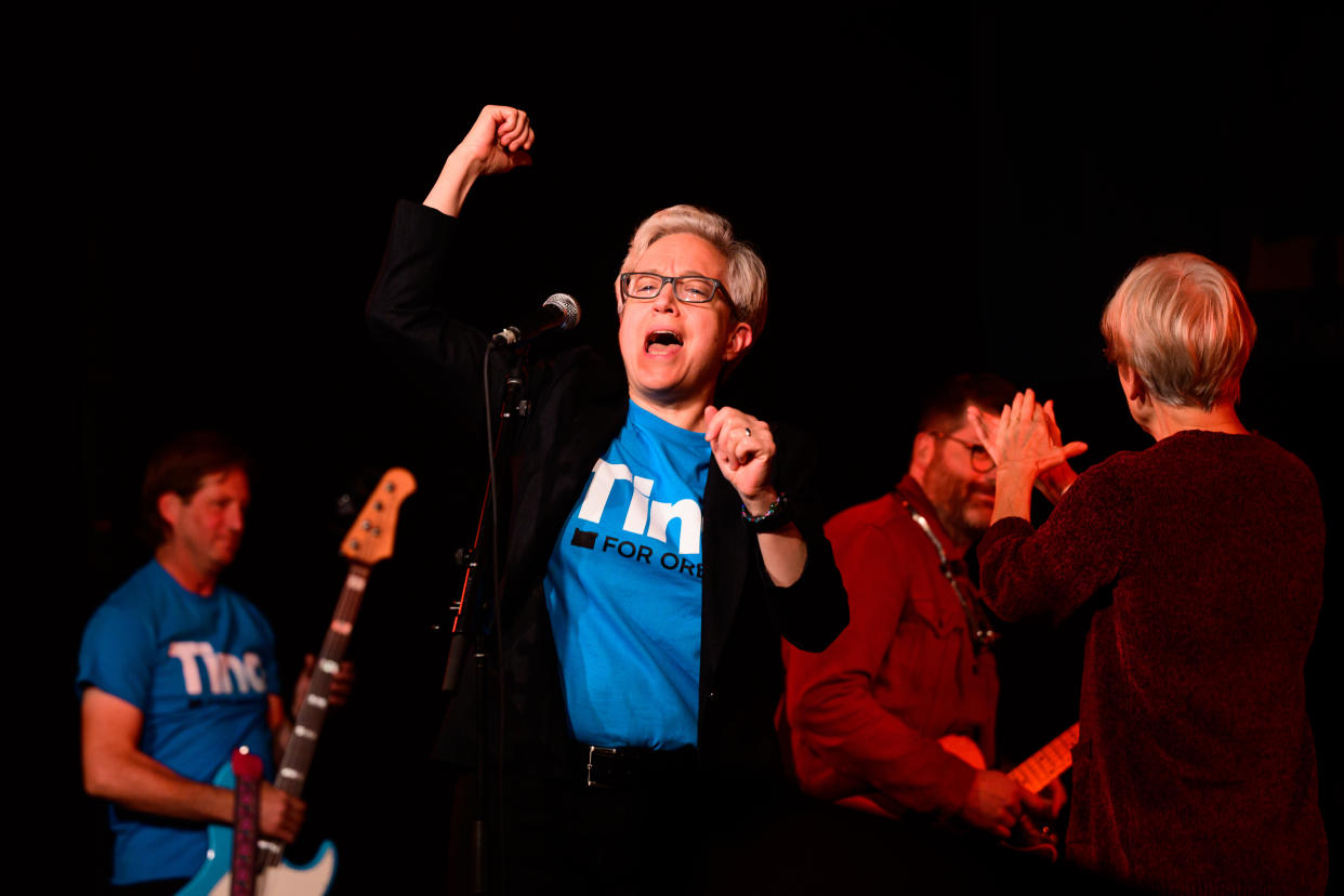 Gubernatorial candidate Tina Kotek, onstage with two guitarists, raises her fist in the air. 