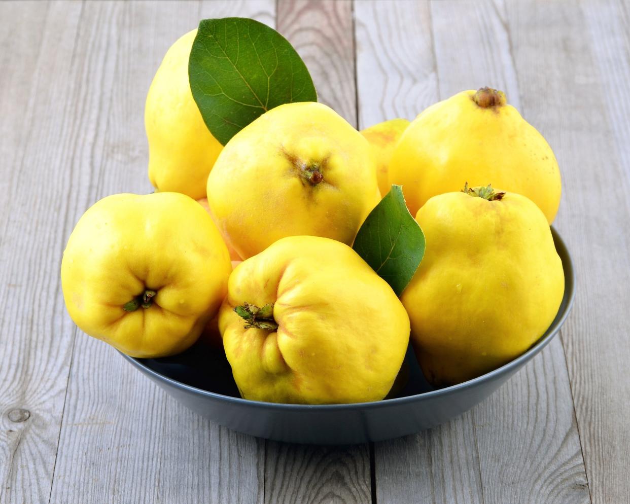 ripe yellow quinces in bowl on wooden table