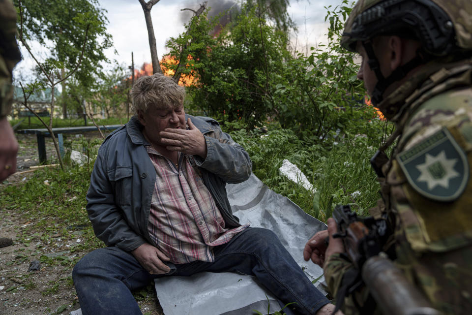 A police officer speaks to a local man as his house is seen on fire after a Russian airstrike in Vovchansk, Ukraine, on Saturday, May 11, 2024. (AP Photo/Evgeniy Maloletka)