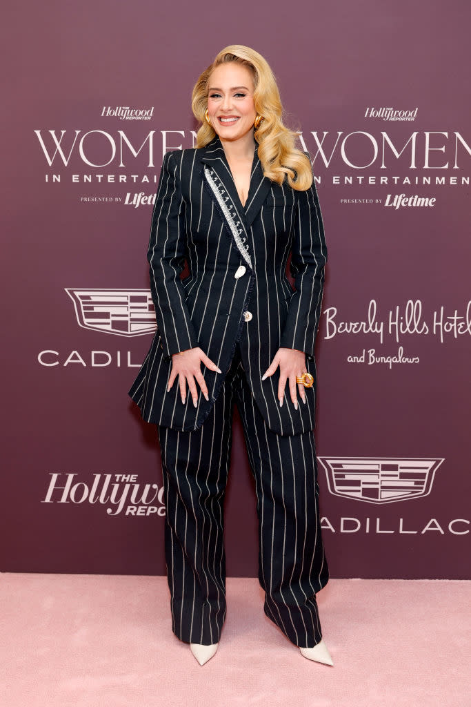 Woman in pinstripe suit with embellished lapel stands smiling at an event