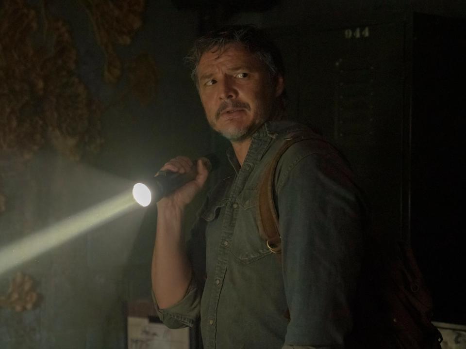 Pedro Pascal wearing a button-down shirt and holding a flashlight in a cave on "The Last of Us"