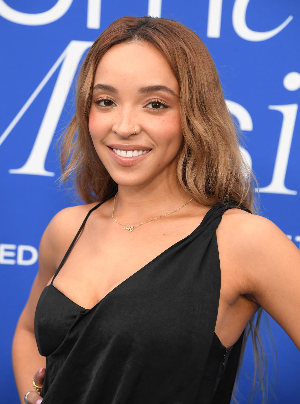 Tinashe poses in a black dress at a formal event with a blue backdrop