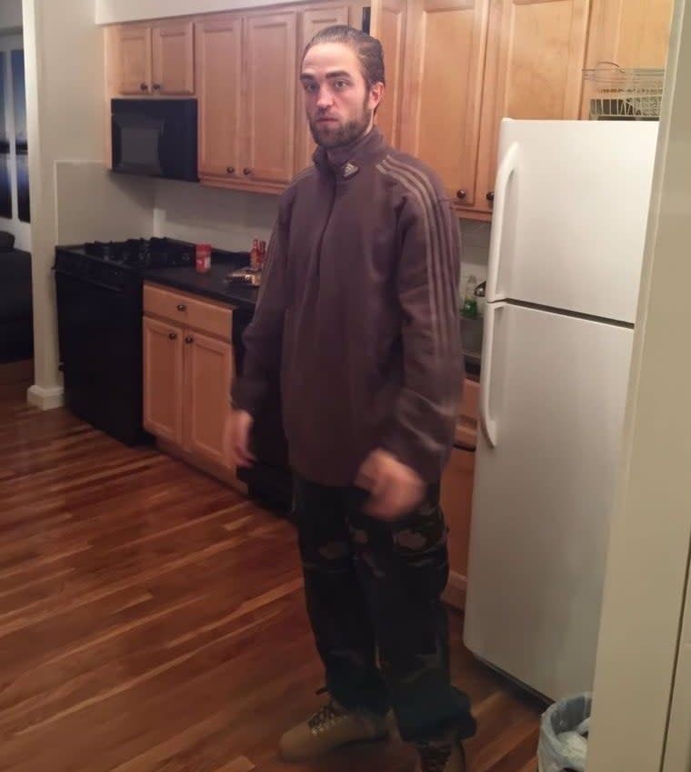 Robert Pattinson standing in a kitchen wearing a brown tracksuit