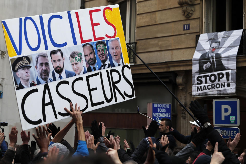 A sign depicting French politicians and reading "Here are the troublemakers" and flags with flares are displayed during the yellow vests 56th round demonstration in Paris, Saturday, Dec. 7, 2019. A few thousand yellow vest protesters marched Saturday from the Finance Ministry building on the Seine River through southeast Paris, pushing their year-old demands for economic justice and adding the retirement reform to their list of grievances. (AP Photo/Francois Mori)