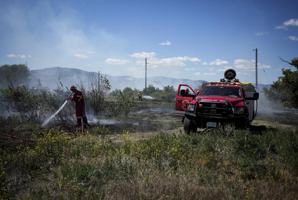 Firefighters battle a grass fire burning on an acreage behind a residential property in Kamloops, British Columbia, Monday, June 5, 2023. No structures were damaged but firefighters had to deal with extremely windy conditions while putting out the blaze. (Darryl Dyck/The Canadian Press via AP)