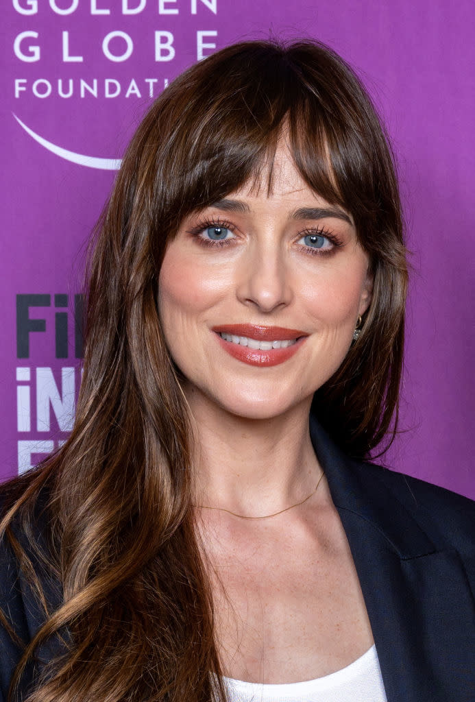 Dakota President at an event, behave a Stygian jacket and a albescent top, grinning at the camera