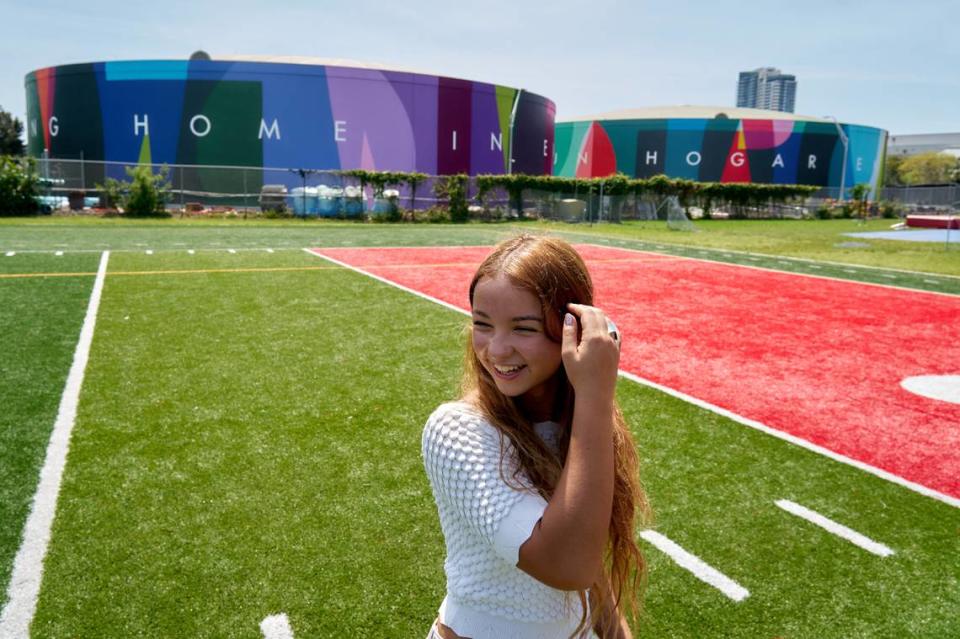 Valentina Mena, a sophomore at Miami Beach Senior High School, in front of the “My Home, Mi Hogar” mural on Friday, May 5, 2023. A line from her poem is featured on the two water tanks. Chantal Lawrie/O, Miami