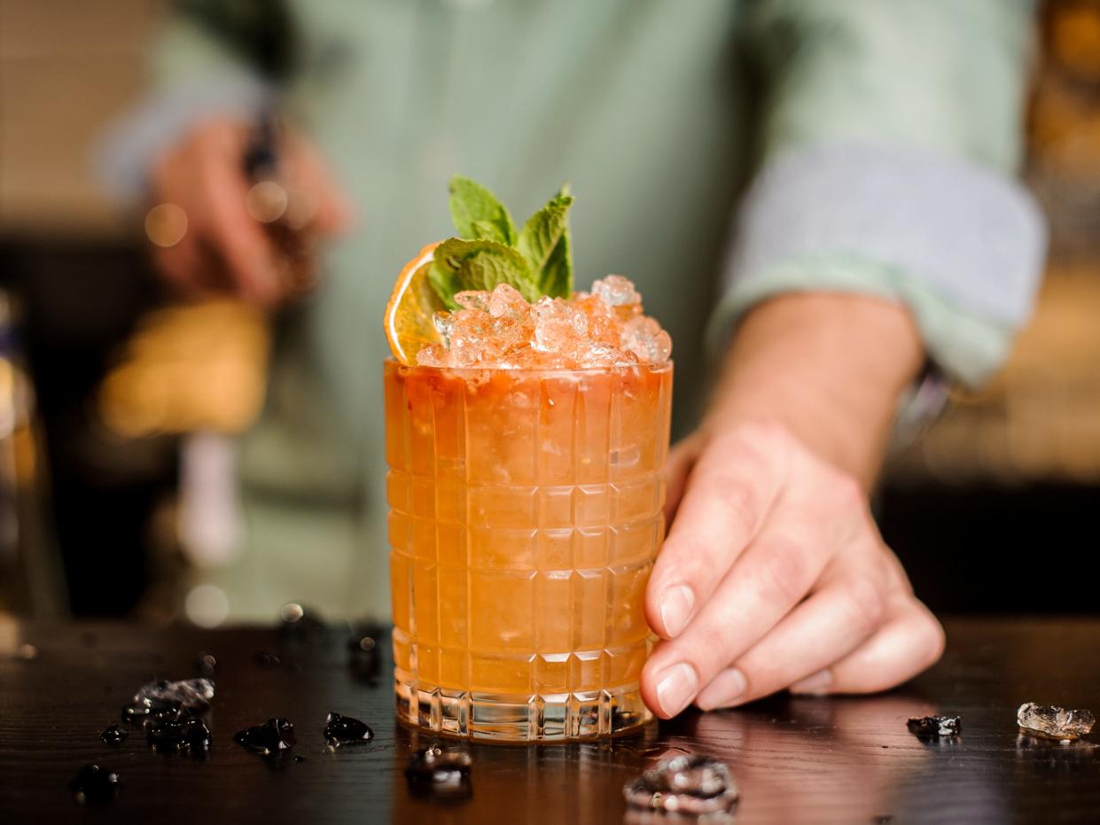 hand pushing an orange fruity cocktail across a bar