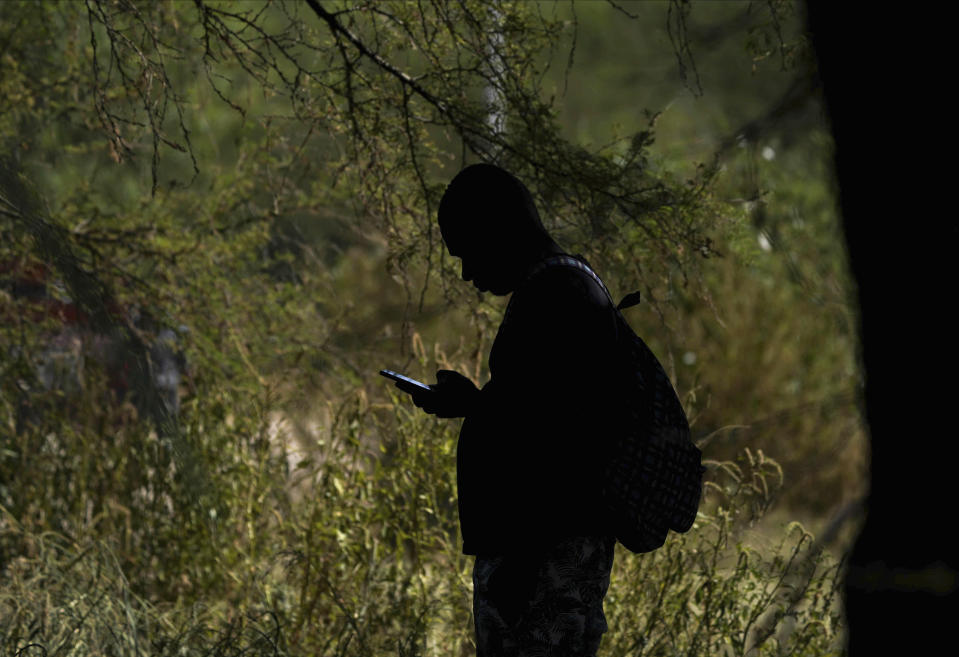 A migrant checks his cellphone at an improvised refugee camp at a sport park in Ciudad Acuña, Mexico, Wednesday, Sept. 22, 2021. (AP Photo/Fernando Llano)