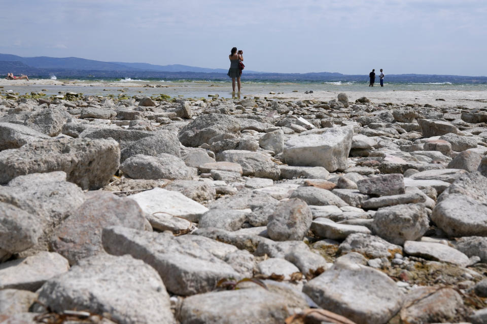 A woman takes pictures in the peninsula of Sirmione, on Garda lake, Italy, Friday, Aug. 12, 2022. Lake Garda water level has dropped critically following severe drought resulting in rocks to emerge around the Sirmione Peninsula. (AP Photo/Antonio Calanni)