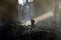 An arson investigator talks on a two-way radio inside a gutted slipper factory in Valenzuela, Metro Manila in the Philippines May 14, 2015. A fire at a factory making rubber slippers killed 31 workers in the Philippine capital on Wednesday, and dozens were missing and feared dead, officials said. REUTERS/Erik De Castro TPX IMAGES OF THE DAY