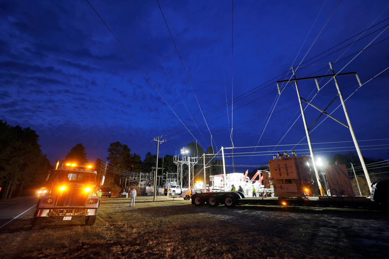 Duke Energy personnel work at dusk to restore power, with a fire truck lighting the surrounding area. 