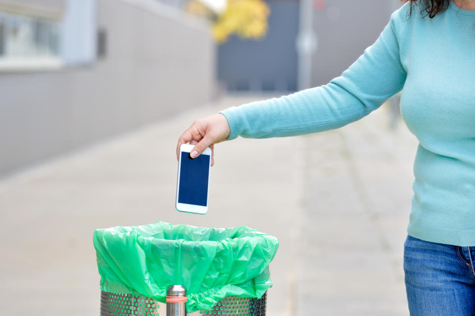 Cropped shot of a hand throwing a phone in the trash with broken screen