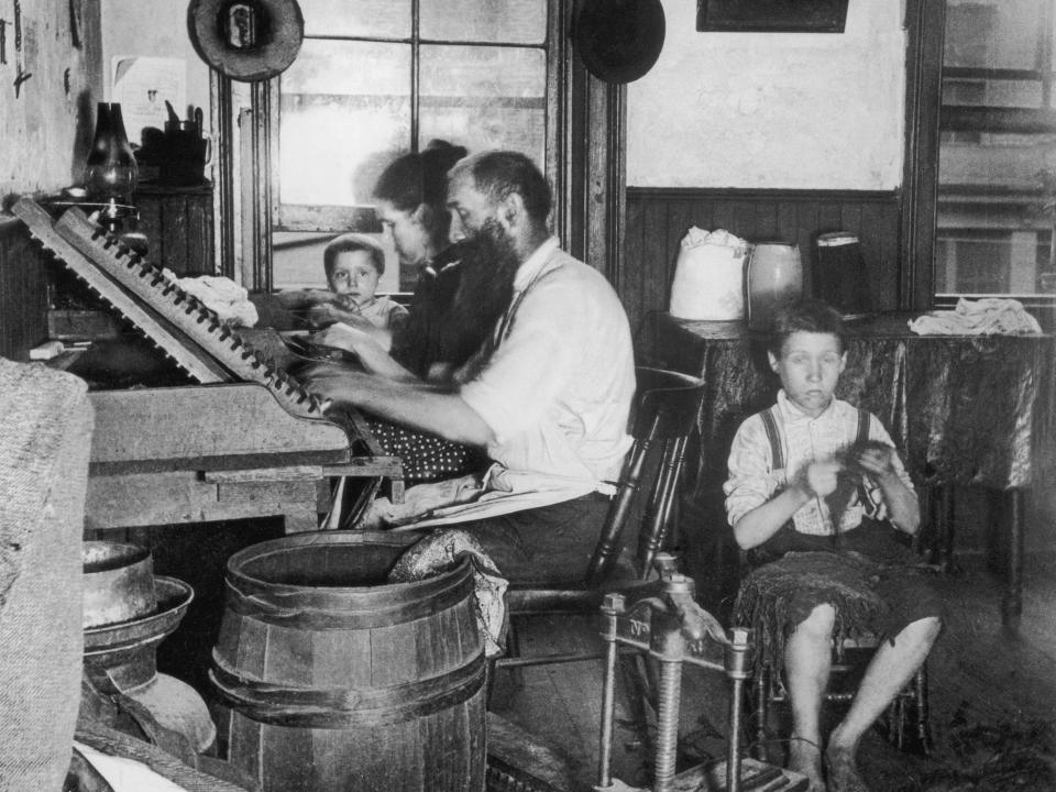 A family of four makes cigars in their home tenement, circa 1890.