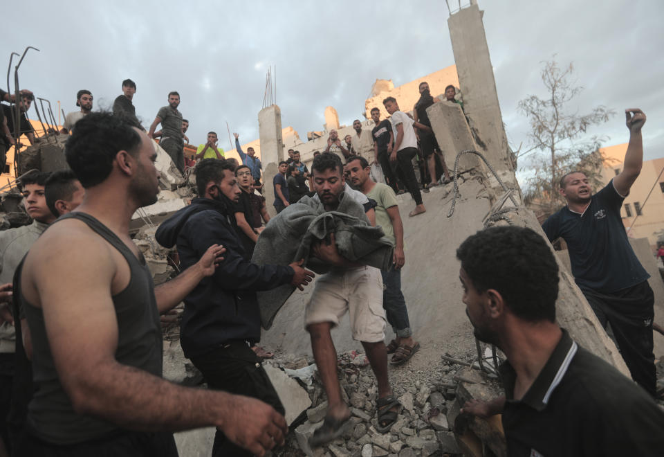 A man carries a blanket covering the remains of a dead person retrieved from the rubble of a house in Khan Younis.