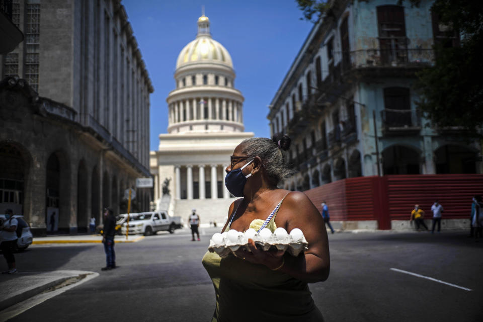 A woman wearing a face mask as a precaution amid the spread of the new coronavirus carries eggs past the Capitol building in Havana, Cuba, Tuesday, June 16, 2020. (AP Photo/Ramon Espinosa)