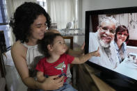 Luna Tarsila points to her grandfather Juracy Cruz Junior, who died of COVID-19, as she sits on the lap her mother, Fernanda Natasha Bravo Cruz, in their home in Brasilia, Brazil, Thursday, Oct. 21, 2021. A Brazilian Senate committee investigating the government’s pandemic response, culminated on Oct. 26, 2021, with the recommendation President Jair Bolsonaro be indicted for crimes, along with dozens of other officials and allies. (AP Photo/Eraldo Peres)