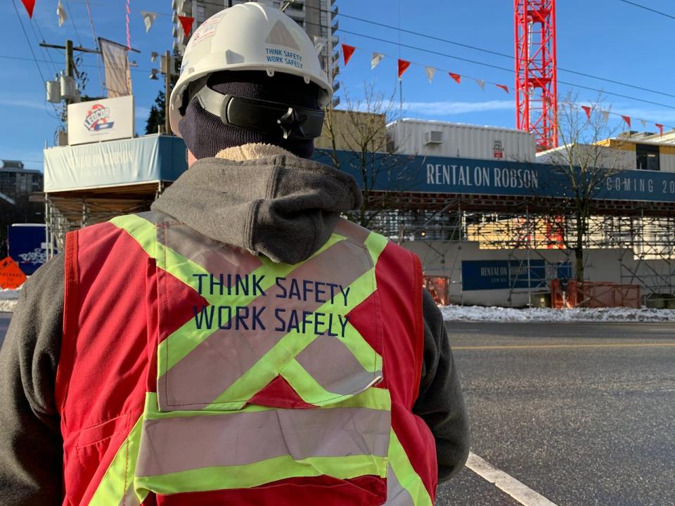 A construction safety officer crosses Robson Street wearing a fluorescent vest with the words; 'Think Safety, Work Safely.' 