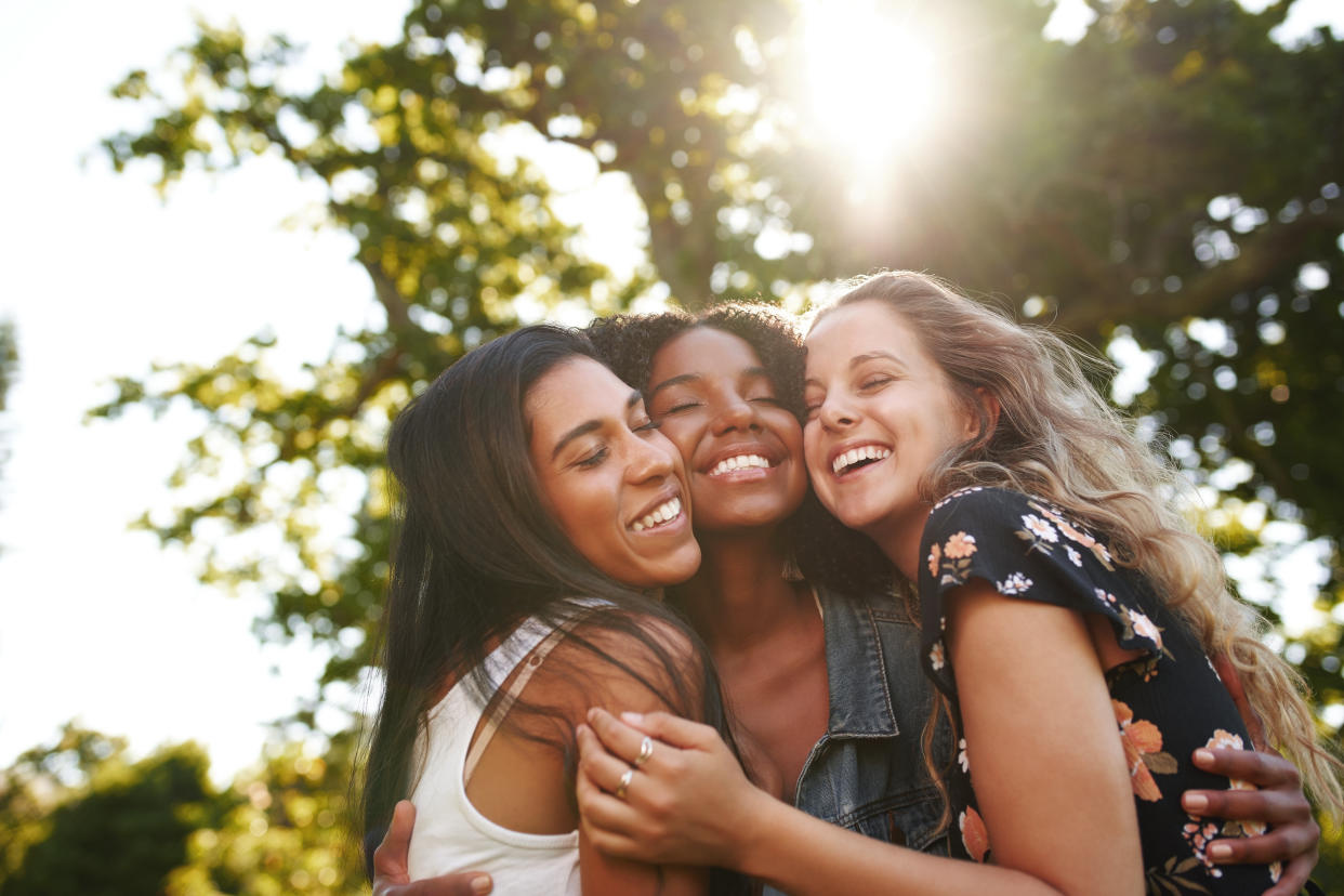 Smiling close group of diverse female best friends hugging each other outdoors in the park on a sunny day - friends showing love