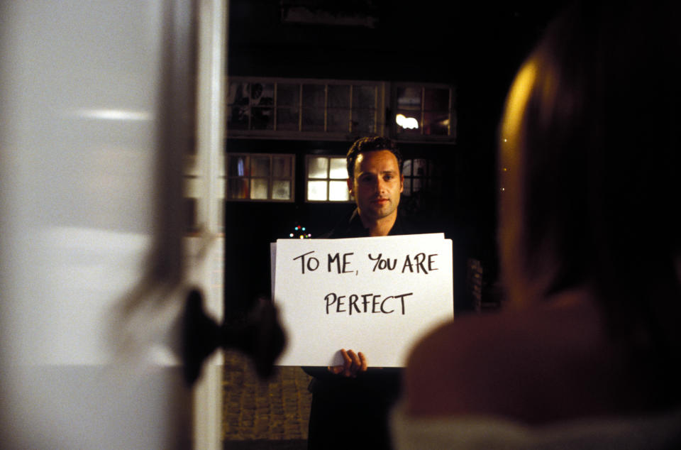 A man holding a sign to a woman saying, "To me, you are perfect"