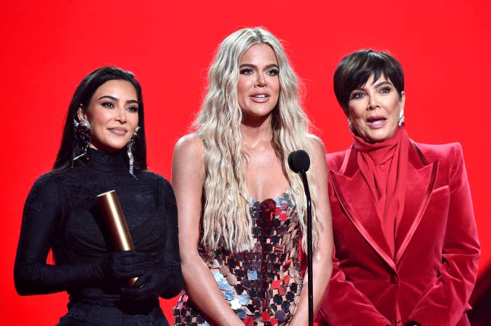 Kim Kardashian, Khloé Kardashian, and Kris Jenner pose together. Kim wears a black outfit, Khloé is in a sequined dress, and Kris is in a red velvet suit