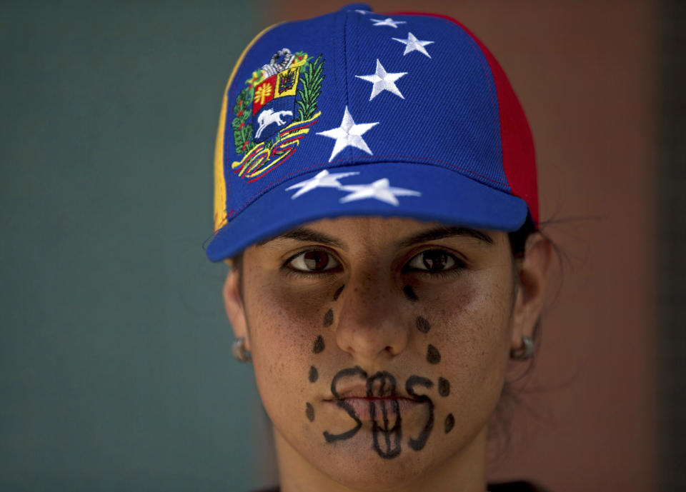 A woman wearing a cap representing Venezuela's national flag, the SOS distress signal marked across her lips and painted black tears streaming down her face, looks into the camera during a demonstration in Caracas, Venezuela, Saturday, March 8, 2014. Venezuelans returned to the streets for the "empty pots march" to highlight growing frustration with shortages of some everyday items. In Caracas, the march was scheduled to end at the country's Food Ministry, but the evening before Caracas' mayor announced that he had not authorized the march. (AP Photo/Fernando Llano)