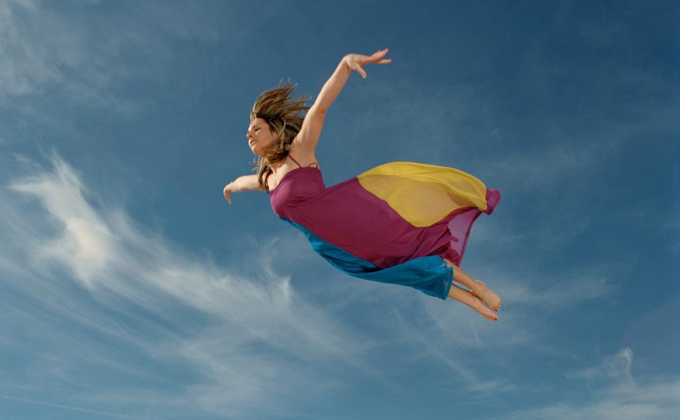 A woman flying in a red and yellow dress.