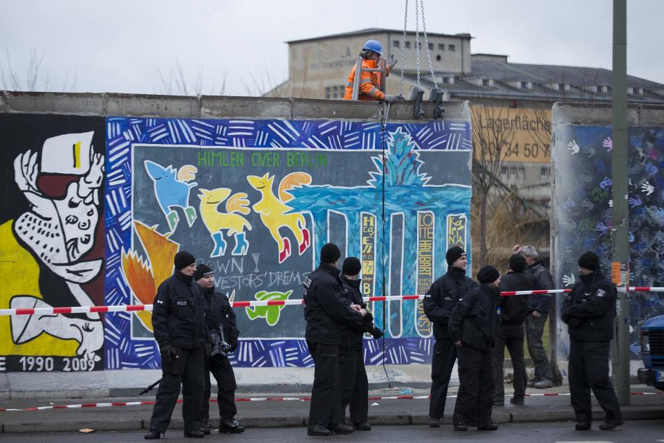 German police officers protect a part of the former Berlin Wall and a construction worker who fixed a part of the wall at a crane in Berlin, Germany, Friday, March 1, 2013. Construction crews stopped work Friday on removing a small section from one of the few remaining stretches of the Berlin Wall to make way for a condo project after hundreds of protesters blocked their path. (AP Photo/Markus Schreiber)