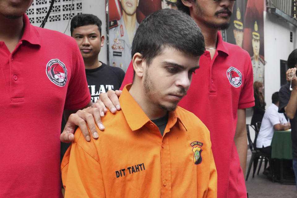 Plain-clothed police officers escort Brazilian national Gustavo Pinto da Silveira prior to a press conference at the regional police headquarters in Jakarta, Indonesia, Wednesday, March 15, 2023. Indonesian authorities said Wednesday they have arrested four foreigners who allegedly tried to smuggle drugs into the country's capital, including da Silveira who was caught with 2 liters (67.6 ounces) of liquid cocaine while arriving from Rio de Janeiro in January, and a Nigerian man who had swallowed dozens of capsules filled with more than a kilogram (2.2 pounds) of methamphetamine. (AP Photo/Tatan Syuflana)