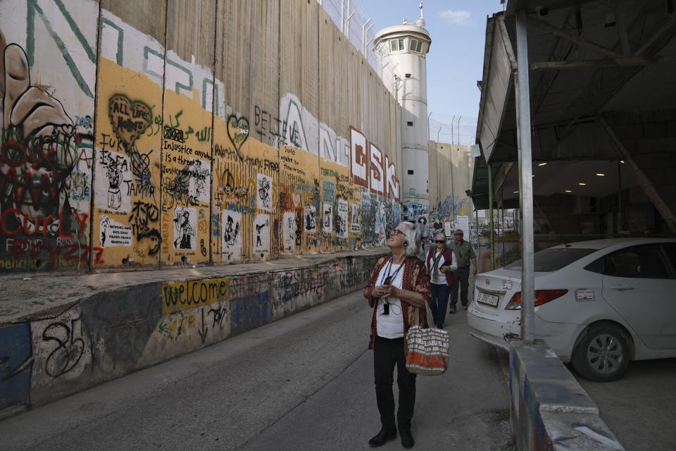 Tourists walk by a section of Israel's separation barrier in the West Bank city of Bethlehem, Monday, Dec. 5, 2022. Business in Bethlehem is looking up this Christmas as the traditional birthplace of Jesus recovers from a two-year downturn during the coronavirus pandemic. Streets are already bustling with visitors, stores and hotels are fully booked and a recent jump in Israeli-Palestinian fighting appears to be having little effect on the vital tourism industry. (AP Photo/ Mahmoud Illean)