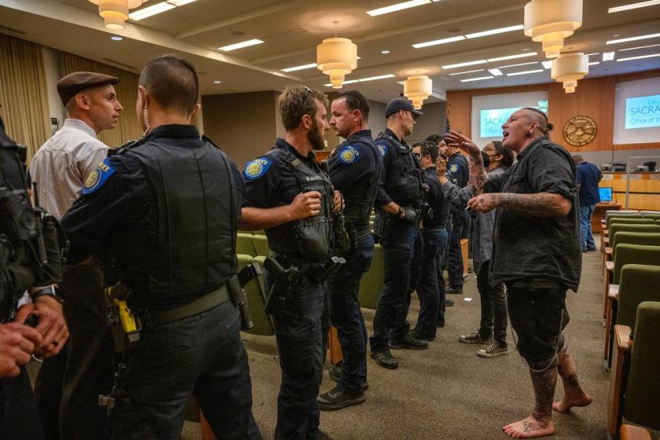 A protester, right, shouts over Sacramento police officers at Ryan Messano, white shirt at left, after the City Council meeting was disrupted by a group calling for Messano’s removal on Tuesday night.