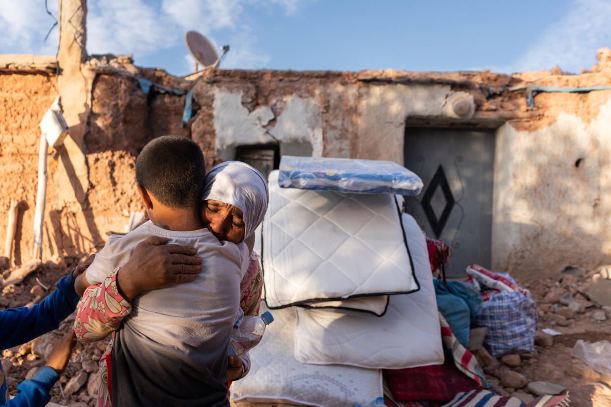 A woman embraces a child outside a damaged structure.