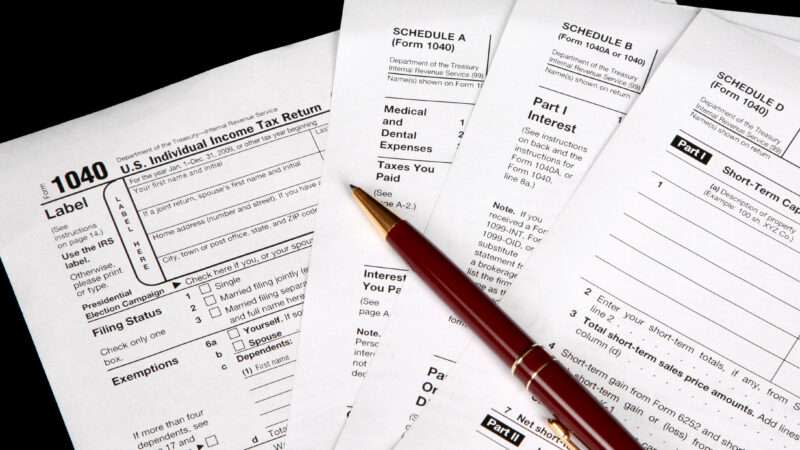 IRS tax forms against a black background, with a ballpoint pen sitting on top.