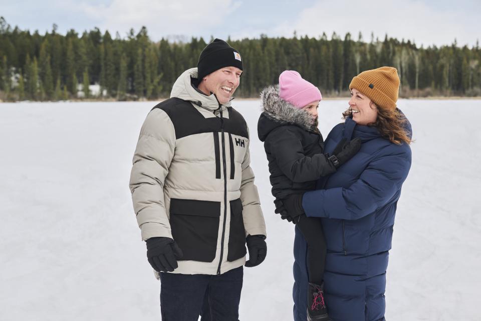 A smiling family is outside enjoying winter weather while bundled up in warm winter jackets and toques.