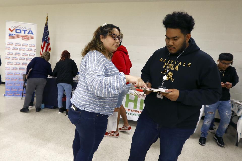 In this March 5, 2020, photo Carmen Martinez, left, of CHISPA Arizona, helps Brian Ramirez, right, with his voter registration form as students participate in their own Democratic presidential preference election and voter registration drive at Maryvale High School in Phoenix. At the school hundreds of students who will turn 18 before Election Day were registered to vote. (AP Photo/Ross D. Franklin)