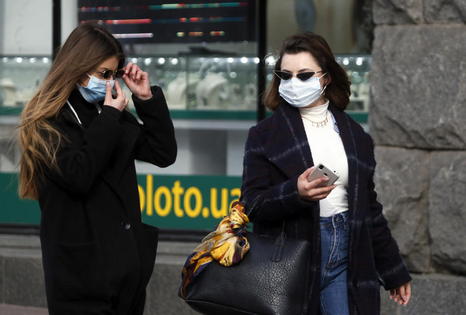 Ukrainians wearing a face masks walk in centrla Kyiv, Ukraine, Monday, March 16, 2020. Ukrainian authorities ruled to close public places except food markets, pharmacies and gas stations starting from Tuesday in Kyiv and seven other regions, and restrict public movement from Kyiv to other Ukrainian cities to strengthen anti-coronavirus quarantine measures. For most people, the new coronavirus causes only mild or moderate symptoms. For some it can cause more severe illness, especially in older adults and people with existing health problems.(AP Photo/Efrem Lukatsky)