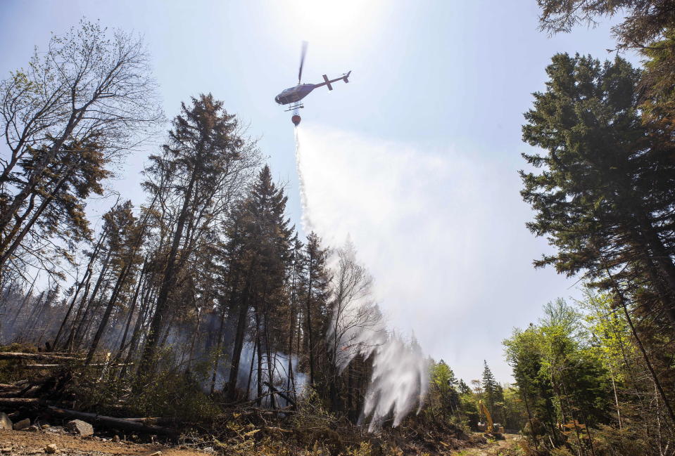 A helicopter contracted by the province drops water on a hot spot in Yankeetown, Nova Scotia, as an excavator makes a fire break, Thursday, June 1, 2023. Rain and a rainy forecast for the weekend have fire officials hopeful they can get the largest wildfire ever recorded in Canada’s Atlantic Coast province of Nova Scotia under control. (Communications Nova Scotia /The Canadian Press via AP)