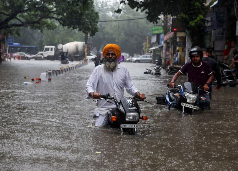 A man on his motorbike wades through a flooded street after heavy rains in New Delhi