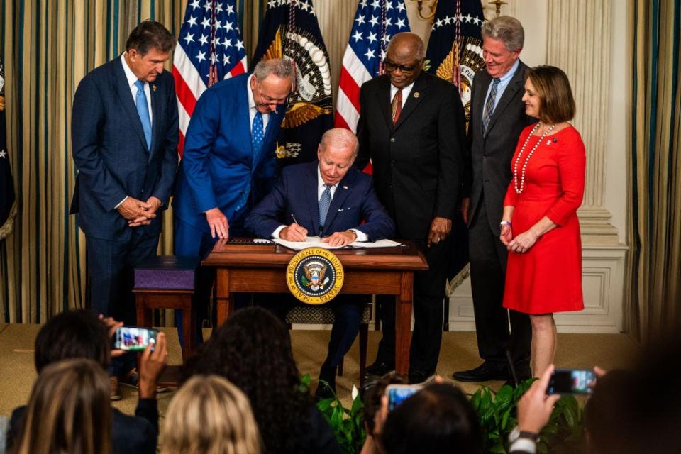 President Joe Biden signs the Inflation Reduction Act into law at the White House surrounded by members of Congress.