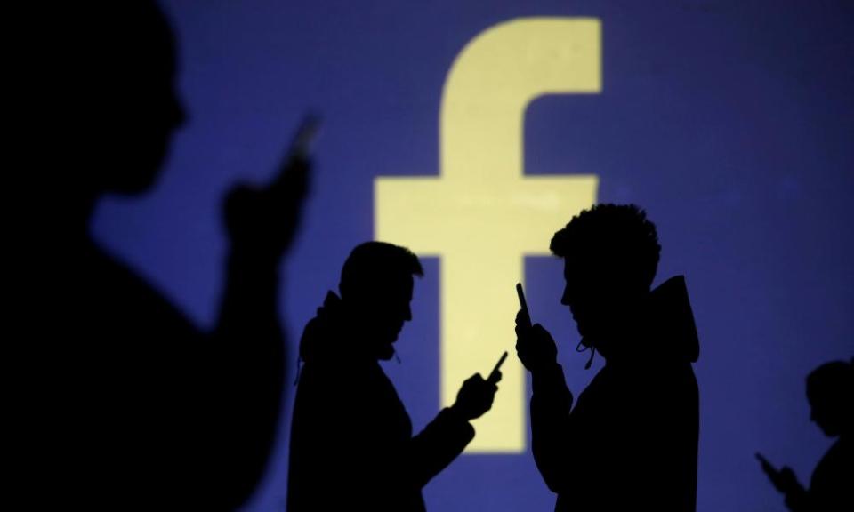 Silhouettes of mobile users are seen next to a screen projection of Facebook logo