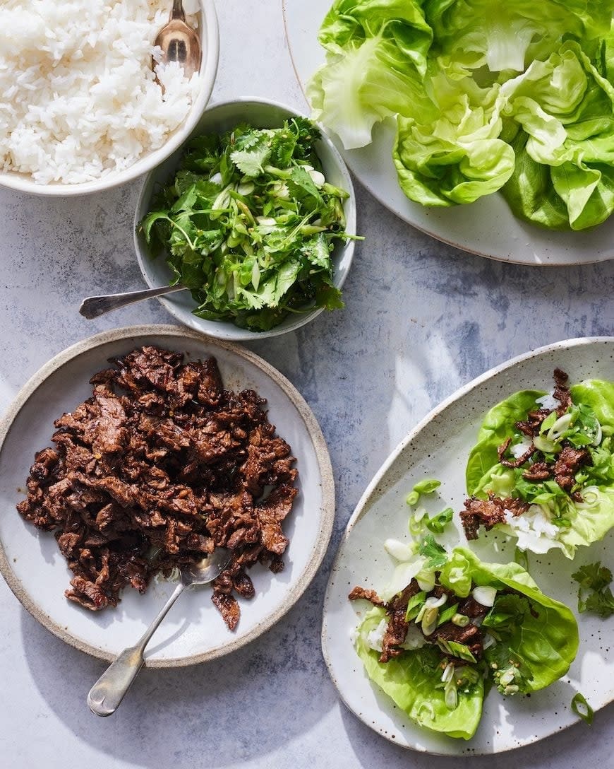 Plates with rice, leafy greens, cilantro salad, and marinated beef arranged for lettuce wraps. A fresh, appetizing meal setting