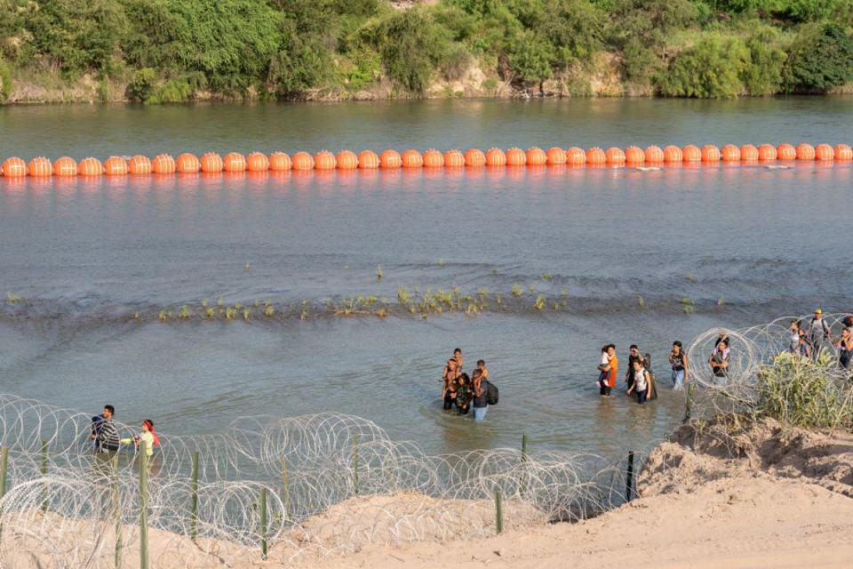 Migrants walk by a string of buoys placed on the water along the Rio Grande border with Mexico in Eagle Pass, Texas (AFP via Getty Images)