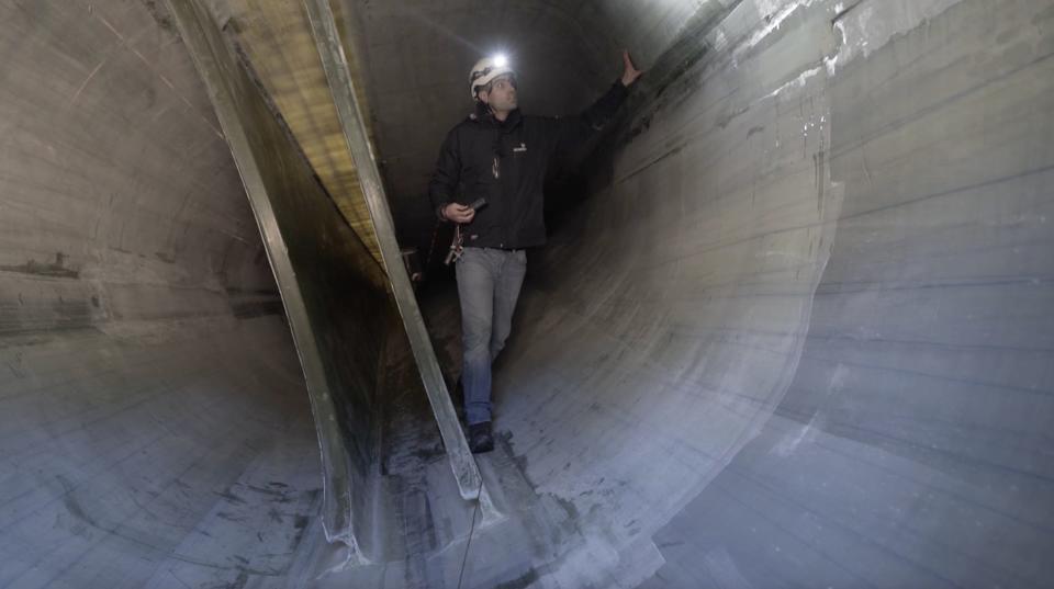 Sardo inside a wind turbine blade with his hand on the blade to examine it.