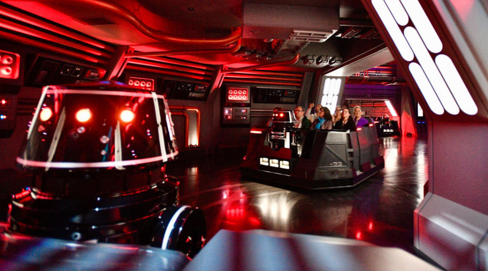 "Visitors experience a space-themed attraction with futuristic control panels and a droid."